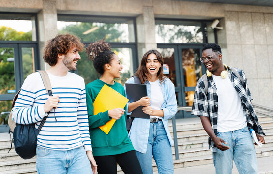 Happy international university friends walking together in campus, chatting and laughing outdoors after school