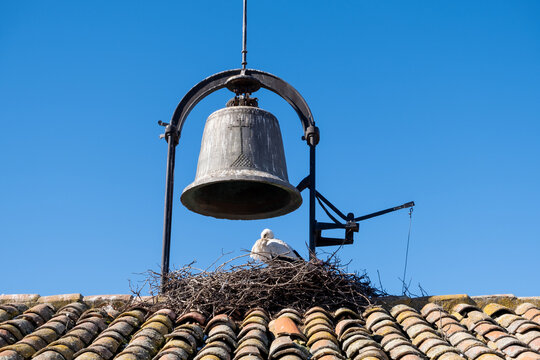 Campana en lo alto del campanario de una peque&ntilde;a iglesia en un pueblo de Castilla y Le&oacute;n con el nido de una cig&uuml;e&ntilde;a y la hembra esperando en &eacute;l.