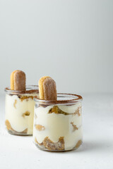 Traditional italian dessert tiramisu with savoiardi biscuits, mascarpone cheese, cream, egg yolks, amaretto liqueur, coffee and cocoa. Portion serving in glass jars. White background, copy space