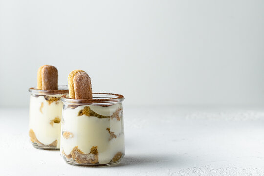 Traditional italian dessert tiramisu with savoiardi biscuits, mascarpone cheese, cream, egg yolks, amaretto liqueur, coffee and cocoa. Portion serving in glass jars. White background, copy space