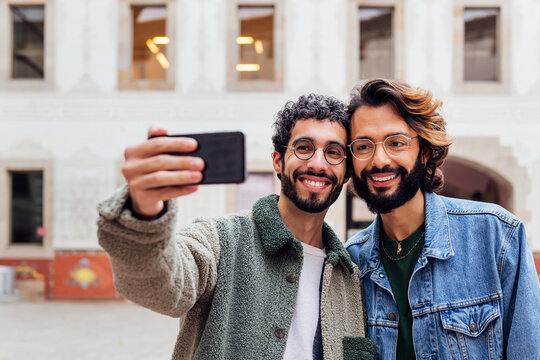 happy couple of gay men taking a selfie photo with their mobile phone in the street, concept of urban lifestyle and love between people of the same sex