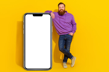 Full length photo of positive person standing near huge empty space phone screen isolated on yellow color background