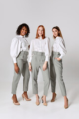Three fashionable stylish young women in office style clothes posing over light background. Concept of beauty, fashion, business
