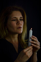 Obraz premium portrait of a beautiful blonde woman blowing out the flame of a candle she is holding