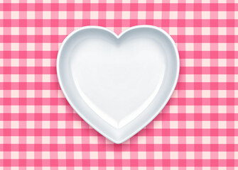 White plate in shape of heart on a pink checkered tablecloth. Clipping path included