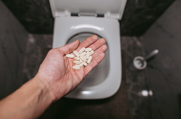 A hand throws pills into the toilet for flushing water