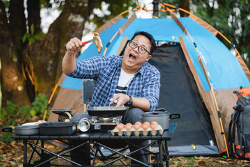 Young male with glasses cooking alone outdoor camping with a tent.