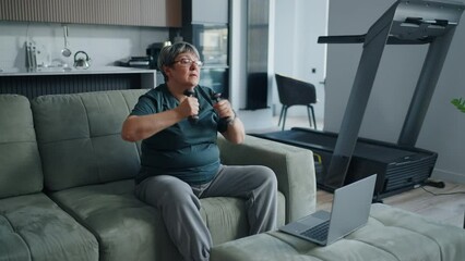Senior Woman Watching Online Sport Training And Doing Physical Exercise At Home, Lifting Dumbbells