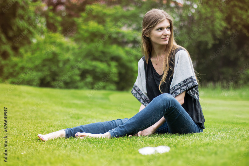 Wall mural smiling girl with long blond hair seating on a summer park lawn