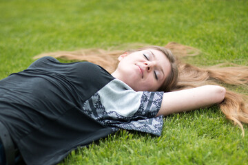 smiling happy playful young woman lying on a park lawn in summer
