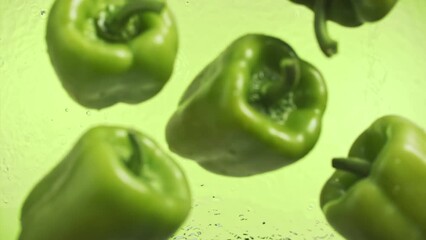 Slow motion of green peppers falling into water surface on green background - Powered by Adobe
