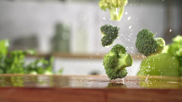Slow motion of fresh green broccoli slices falling on wet wooden board in a kitchen