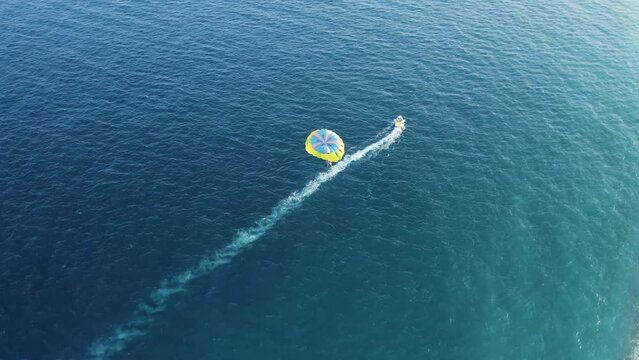 Aerial view of a person doing parasail with a motorboat along the coast in Sicily, Italy.
