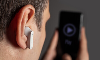 A man in wireless headphones listens to music on a smartphone.
