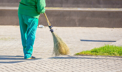 The janitor cleans the city street with a broom in the city. Street cleaning service. A worker...