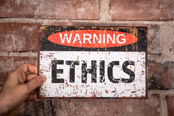 Ethics Concept. Warning sign with text in hand of woman. Red brick background