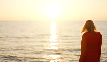 Woman in red dress looks at the sunset on the seashore.