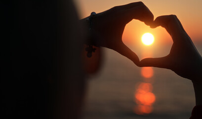 Female hands making heart shape in the sunset.