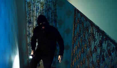 Thief in a balaclava at night in the house. - obrazy, fototapety, plakaty