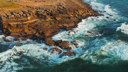 Fototapeta na wymiar Ocean waves rolling to the rocky shore. Beautiful seascape. Aerial top view of the beautiful ocean rocky shore with rolling waves. Drone is hovering over rolling ocean waves to rocky shore