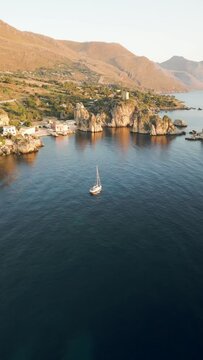 Vertical aerial view of a small sailing boat sailing along Marina Piccola beach in Capri Island, Naples, Campania, Italy.