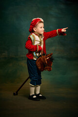 One cute little boy dressed up as medieval little prince and pageboy ride toy horse over dark...