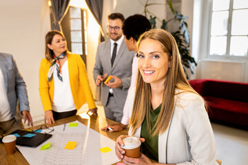 Portrait of smiling businesswoman in office with her colleagues in background.