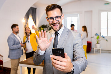 Fototapeta premium Portrait of smiling businessman in office using smartphone for video call.