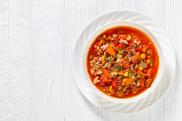 Easy hot and hearty Hamburger Soup with barley and vegetables in white bowl on white wood table