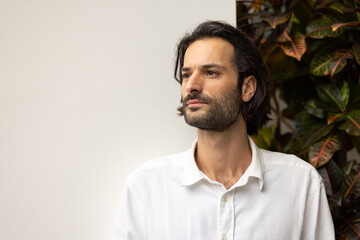 portrait d'un jeune homme de 30 ans beau et souriant. En arrière plan, il y a des plantes vertes et un bureau confortable