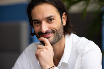 portrait d'un jeune homme de 30 ans beau et souriant. En arrière plan, il y a des plantes vertes...