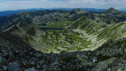 Panorama above the high summits of Retezat Mountains and the glacier Bucura lake beneath them. High altitude landscape with rocky mountains and alpine pastures. Carpathia, Romania.
