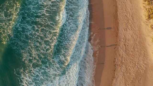 Aerial view of a person walking on the beach along the shoreline at Constantine Bay at sunset, Cornwall, United Kingdom.
