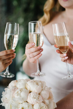 Young bridesmaids clinking with glasses of champagne in hotel room. Closeup photo of cheerful girls celebrating a bachelorette party. Females have toast with white wine.