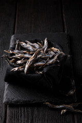Dried anchovies on a stone board on a dark wooden table, side view.