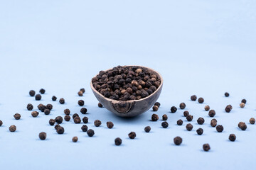 A wooden bowl filled with black pepper. A wooden bowl filled with black pepper in a minimalist style. Front view. Scattered black pepper