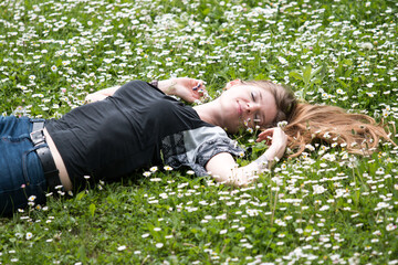 smiling young woman lying on a lawn with daisies in summer field