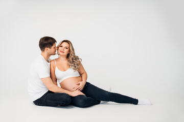 a couple waiting for a child sit on the floor of a cyclorama in a photo studio 