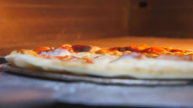 Male cook putting pizza in the oven using a shovel and closing it at cuisine restaurant. Young chef is going to bake delicious dish in furnace at kitchen. Process of making food at pizzeria. Close up