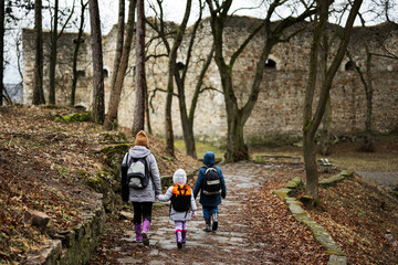 Fototapeta premium Back of mother and kids walk path to an ancient medieval fortress in rain. Terebovlia castle, Ukraine.
