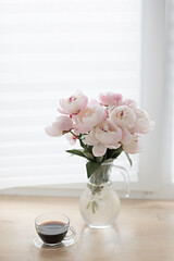 Bouquet of pink peonies and a cup of coffee. Modern interior in the kitchen. Wedding and festive style.