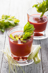 Tomato juice in a glass with celery on a light wooden table, side view.