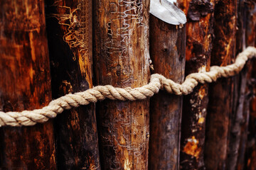 Fragment of an old log fence decorated with decorative rope. Close up