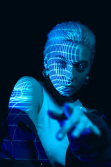 Deep look. Portrait of young blonde girl with neon stripes on face posing over dark background in...