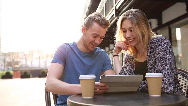 Happy young couple having a coffee together and looking at a digital tablet