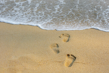 Keep walking and moving forward concept with footprints of human feet walked on the white sand beach with the wave approaching shore, Sand texture, Nature background.