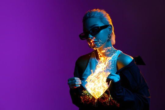 Burning inside. Portrait of young blonde girl with digital fire on body posing over purple background in blue neon lights. Concept of art, modern style, cyberpunk, futurism and creativity