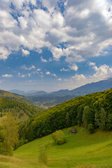 Fototapeta na wymiar Rural idyllic landscape with grassy fields and rolling hills, sunny afternoon, dramatic sun rays piercing the fluffy clouds. Wonderful springtime landscape in mountains. Nature freshness concept