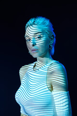 Abstract art. Portrait of young blonde girl with neon stripes on face posing over dark background...