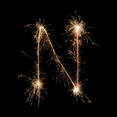 Sparkling burning creative letter N isolated on black background. Beautiful glowing golden overlay object for design holiday greeting card. Creative lettering N written with burning sparklers